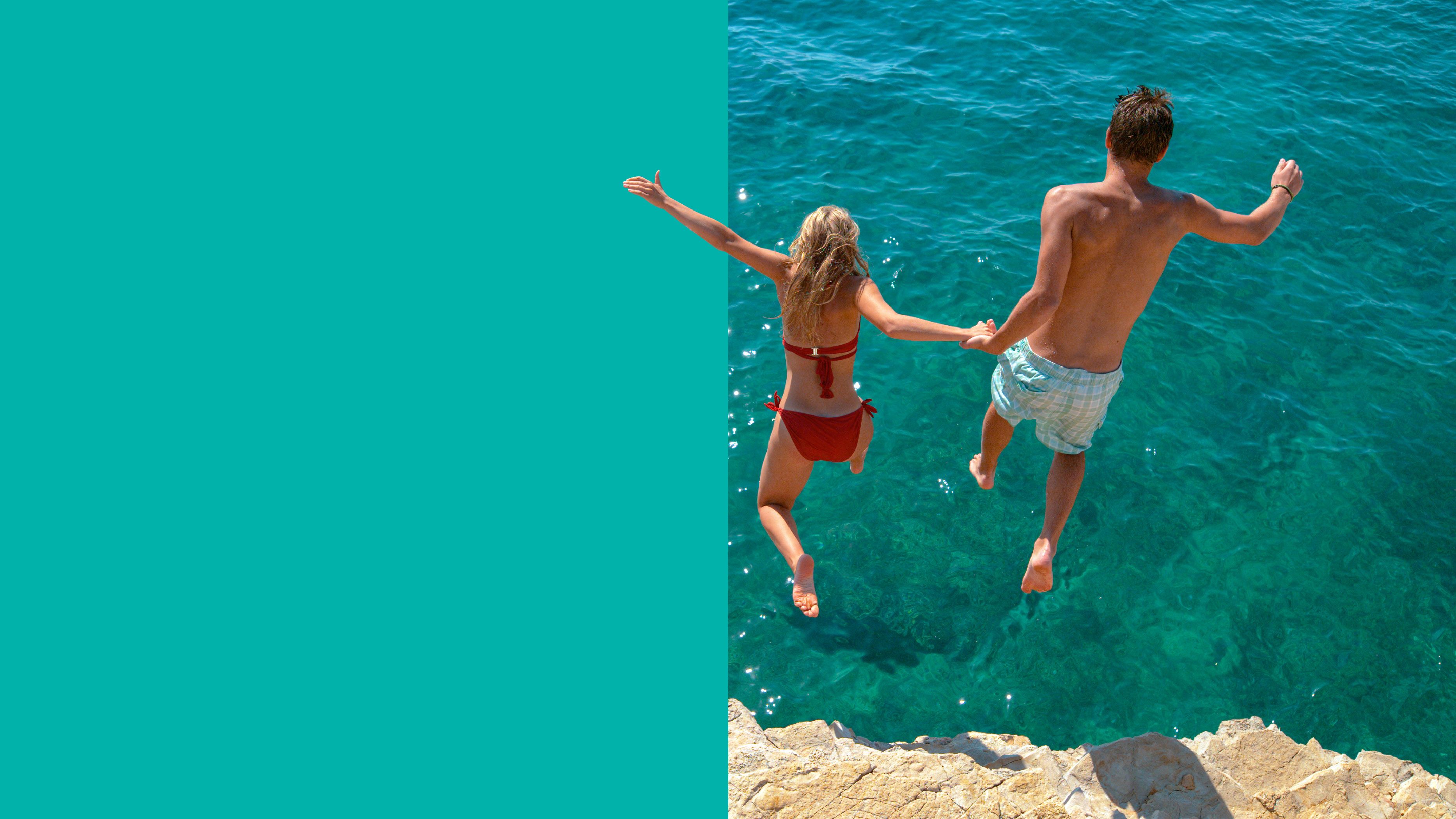couple jumping into turquoise ocean 